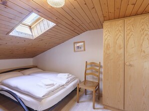Ein Schlafzimmer mit einem Bett, einem Holzstuhl, einem Kleiderschrank und einem Dachfenster.