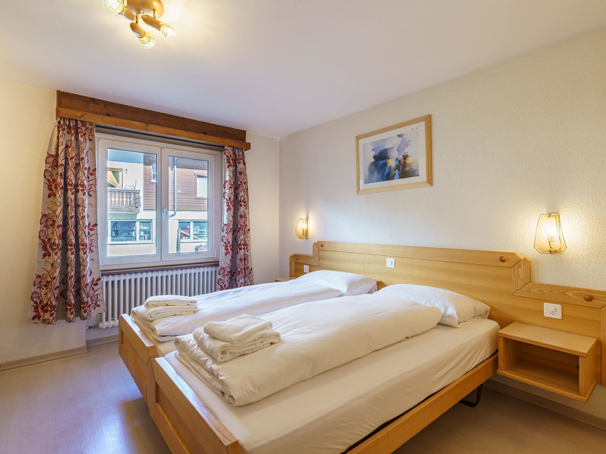 Une chambre d’hôtel avec un lit, deux tables de chevet, une fenêtre avec des rideaux, un radiateur et un tableau au mur.