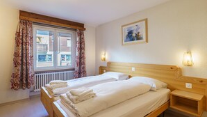Ett hotellrum med en säng, två sängbord, ett fönster med gardiner, ett element och en tavla på väggen.