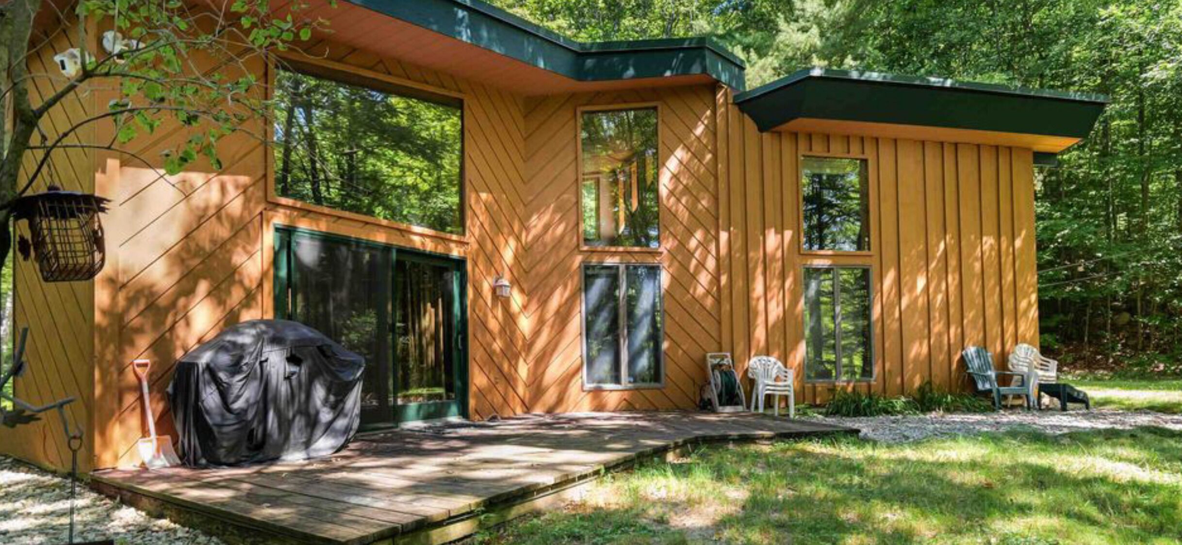 Una cabaña de madera moderna con un porche cubierto, ventanas amplias y mobiliario de exterior.