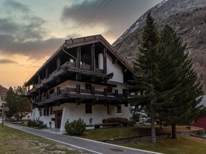 Ein mehrstöckiges Gebäude mit Balkon, umgeben von Bäumen und mit Blick auf einen Berg.