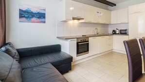 Een moderne keuken met witte kasten, een inbouwoven, en een zithoek met een leren zwarte bank en een stoel.