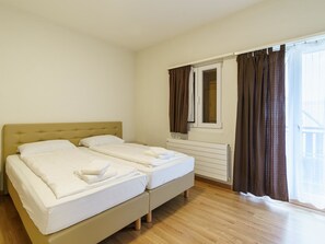 A hotel room with two beds, a window with curtains, a radiator, and wooden flooring. - Haus Astoria by Interhome (Saas-Grund)