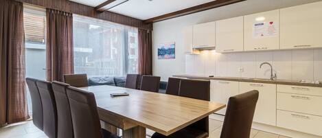 A modern kitchen with white cabinets, a stainless steel sink, and a dining area with a wooden table and leather chairs.