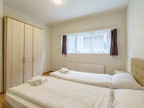 A hotel room with a large wardrobe, a bed with white linens, a window with sheer curtains, and a headboard. - Haus Astoria by Interhome (Saas-Grund)