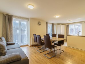 Ein modernes Wohnzimmer mit einer Couch, einem Esstisch und Stühlen. Es gibt eine Küchenzeile mit Spüle und Schränken.