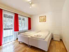 A bedroom with a bed, a nightstand, a radiator, and a window with curtains. - Haus City by Interhome (Saas-Grund)