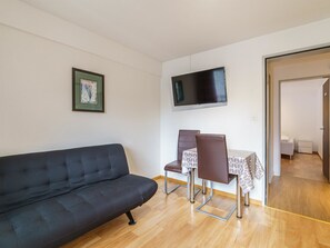A modern living room with a black sofa, a dining table with two chairs, a flat-screen TV mounted on the wall, and a framed picture on the wall. - Haus City by Interhome (Saas-Grund)