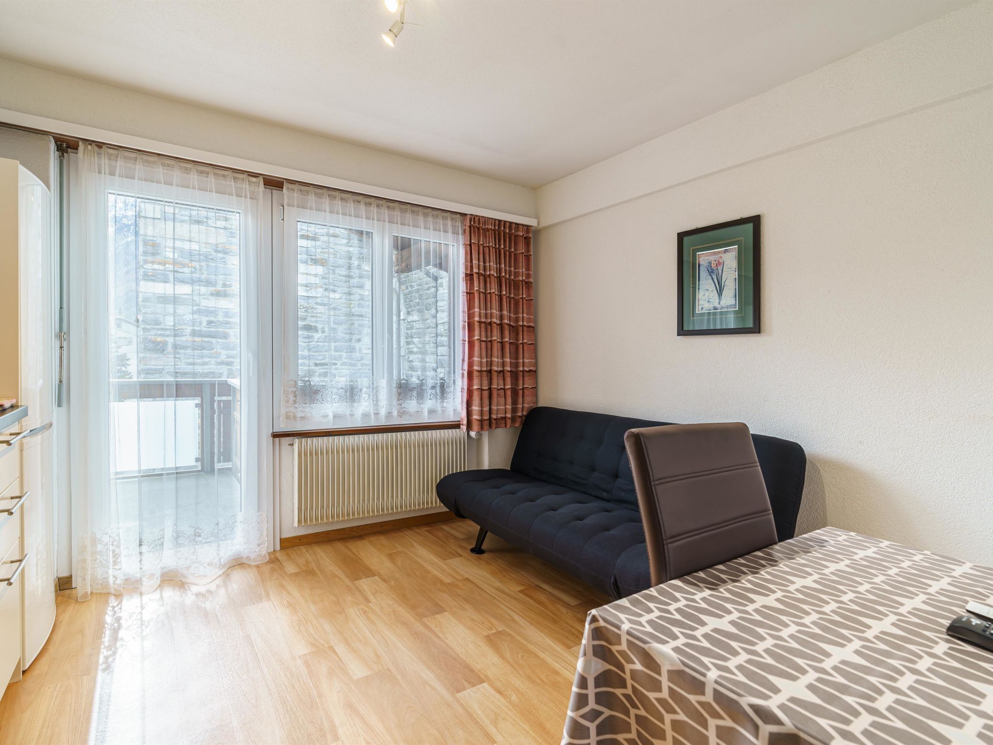A room with a sofa, a table, a radiator, and a window with curtains.