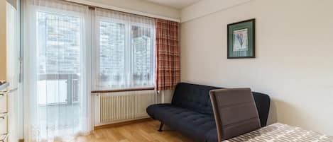 Una habitación con sofá, una mesa, un radiador y una ventana con cortinas.