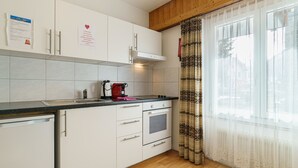 Eine moderne Küche mit weißen Schränken, einer Edelstahl-Spüle, einem eingebauten Backofen und einem Fenster mit gemusterten Vorhängen.