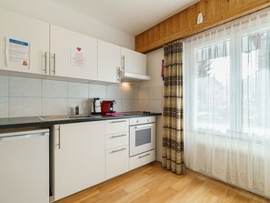 Eine moderne Küche mit weißen Schränken, einer Edelstahl-Spüle, einem eingebauten Backofen und einem Fenster mit gemusterten Vorhängen.