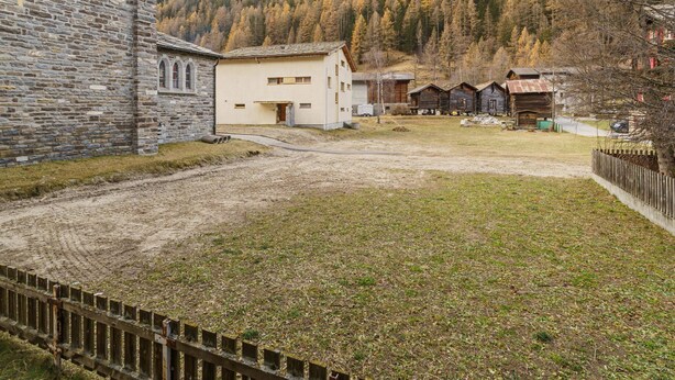 Ein Steinhaus mit weißer Fassade, ein kleines weißes Gebäude und mehrere Holzhütten in einer gebirgigen Landschaft.