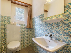 Un bany amb rajoles amb motius, un vàter, un lavabo i una finestra amb cortina.