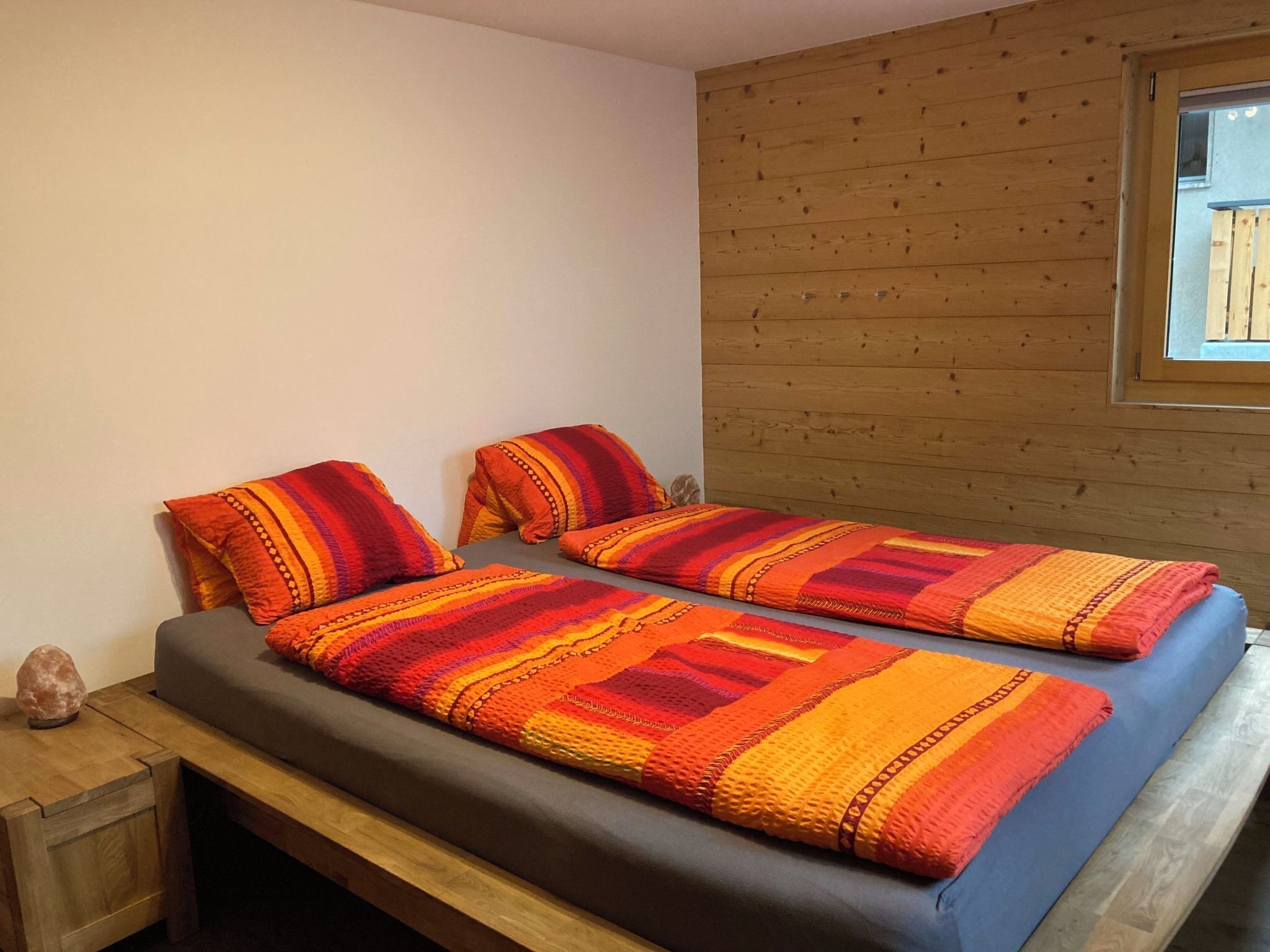 Ein Zimmer mit einem Bett, zwei Kissen, einer Holzwand und einem Fenster.