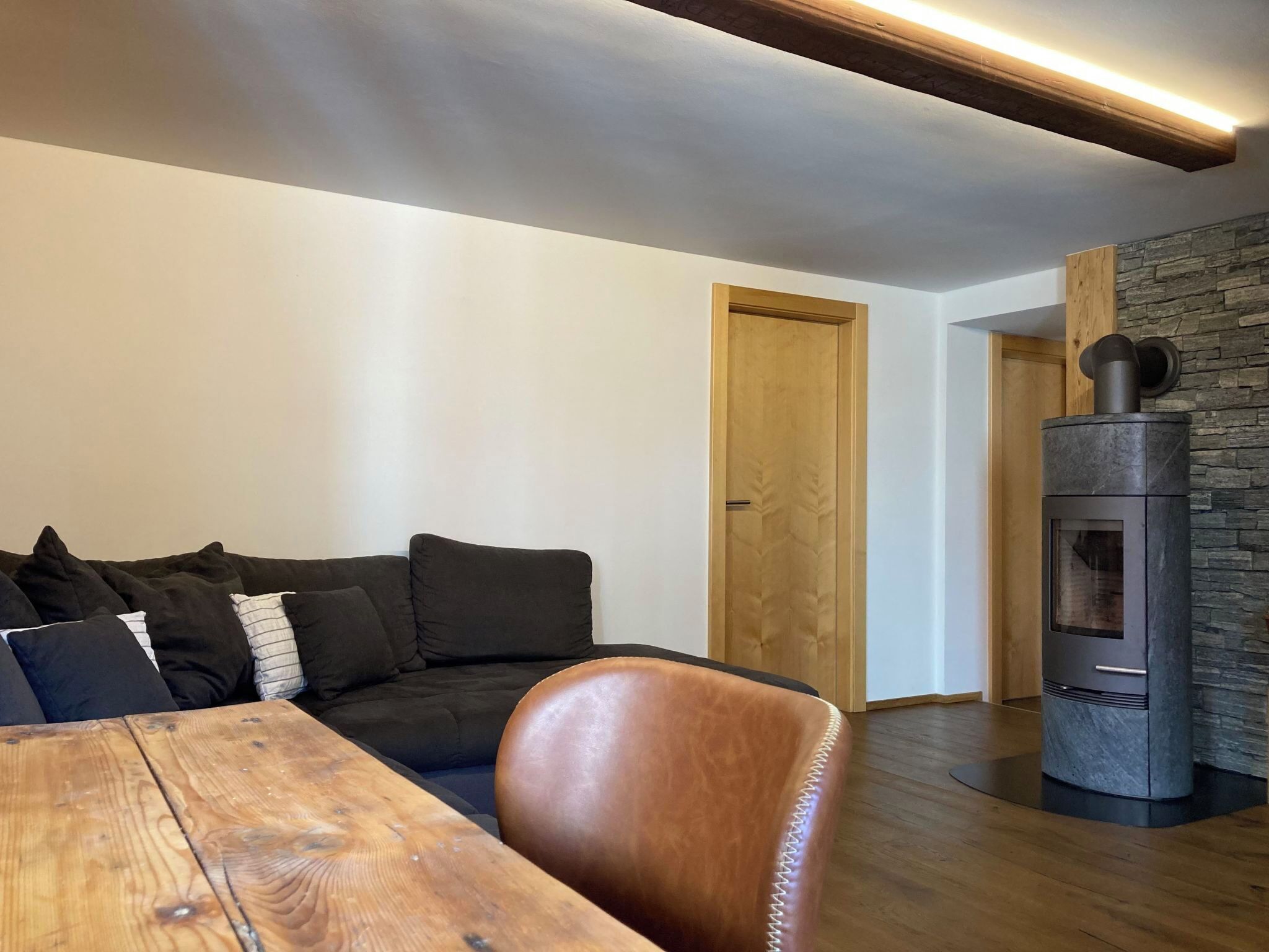 Un salon moderne avec une table en bois, un canapé noir et un mur en pierre.