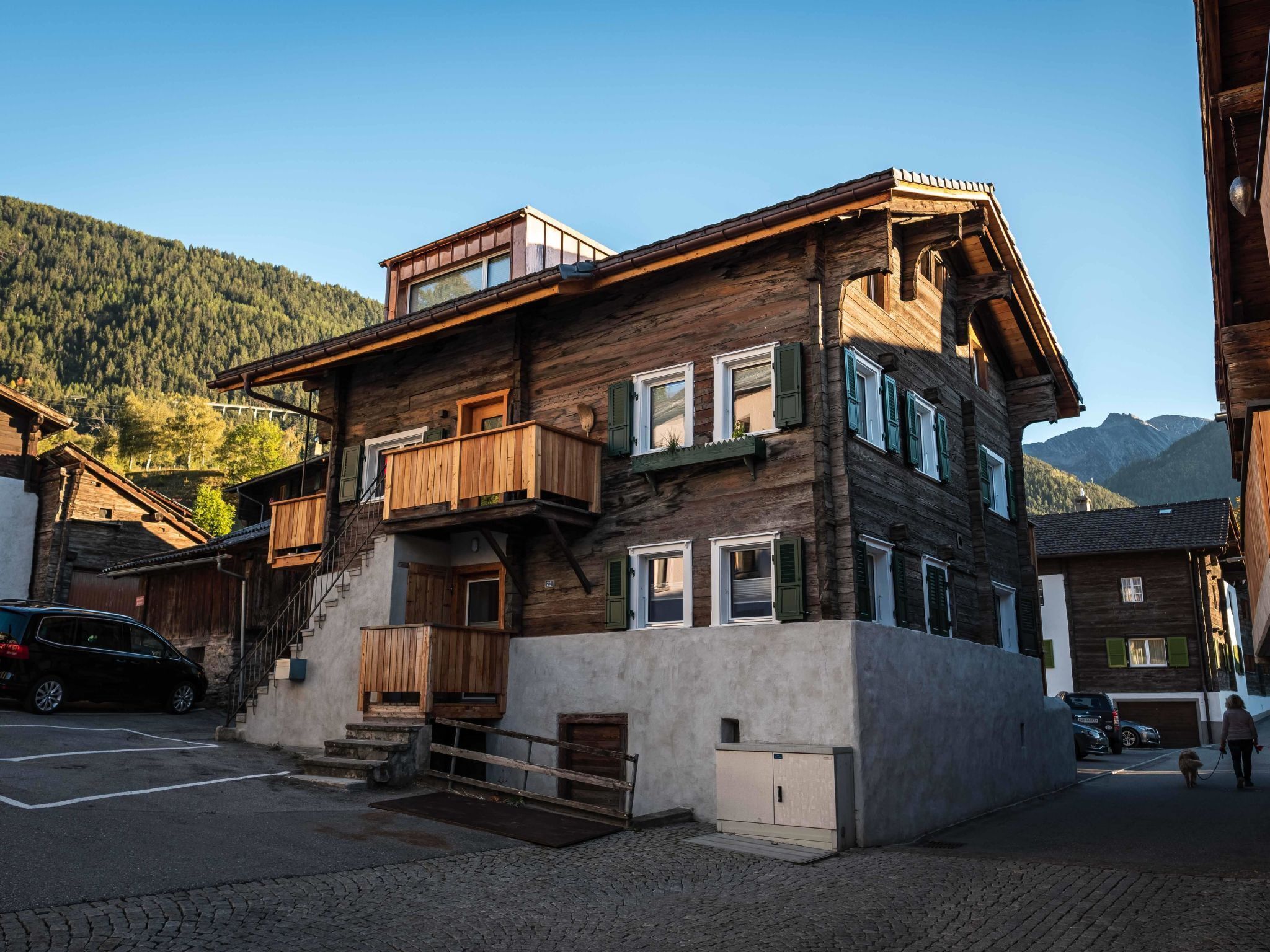Un immeuble en bois à plusieurs étages, doté de balcons, d’un escalier et d’une voiture garée devant.