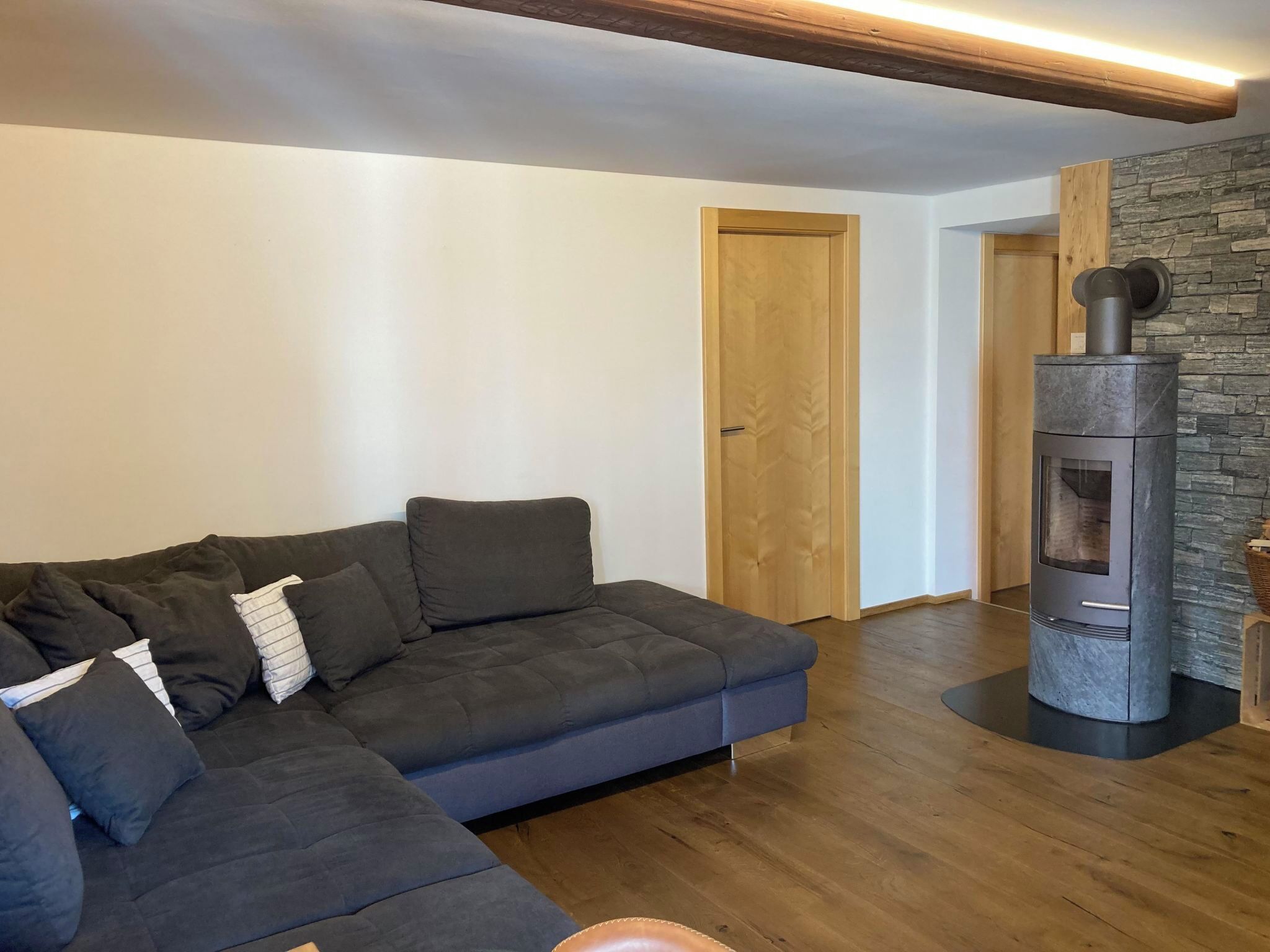 Una sala de estar moderna con un sofá seccional gris oscuro, una pared de piedra y un estufa de leña.