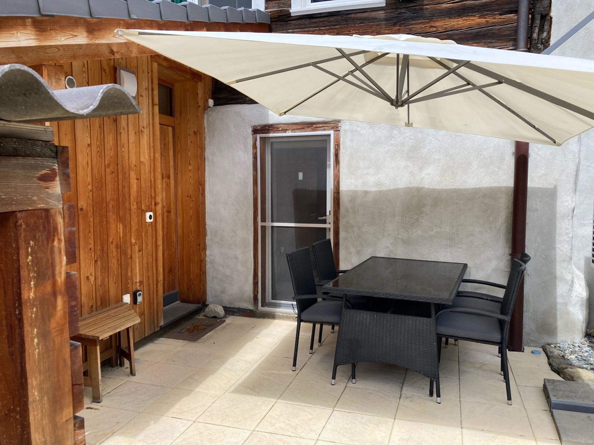Un patio con una mesa, sillas, una estructura de madera y una puerta de cristal.