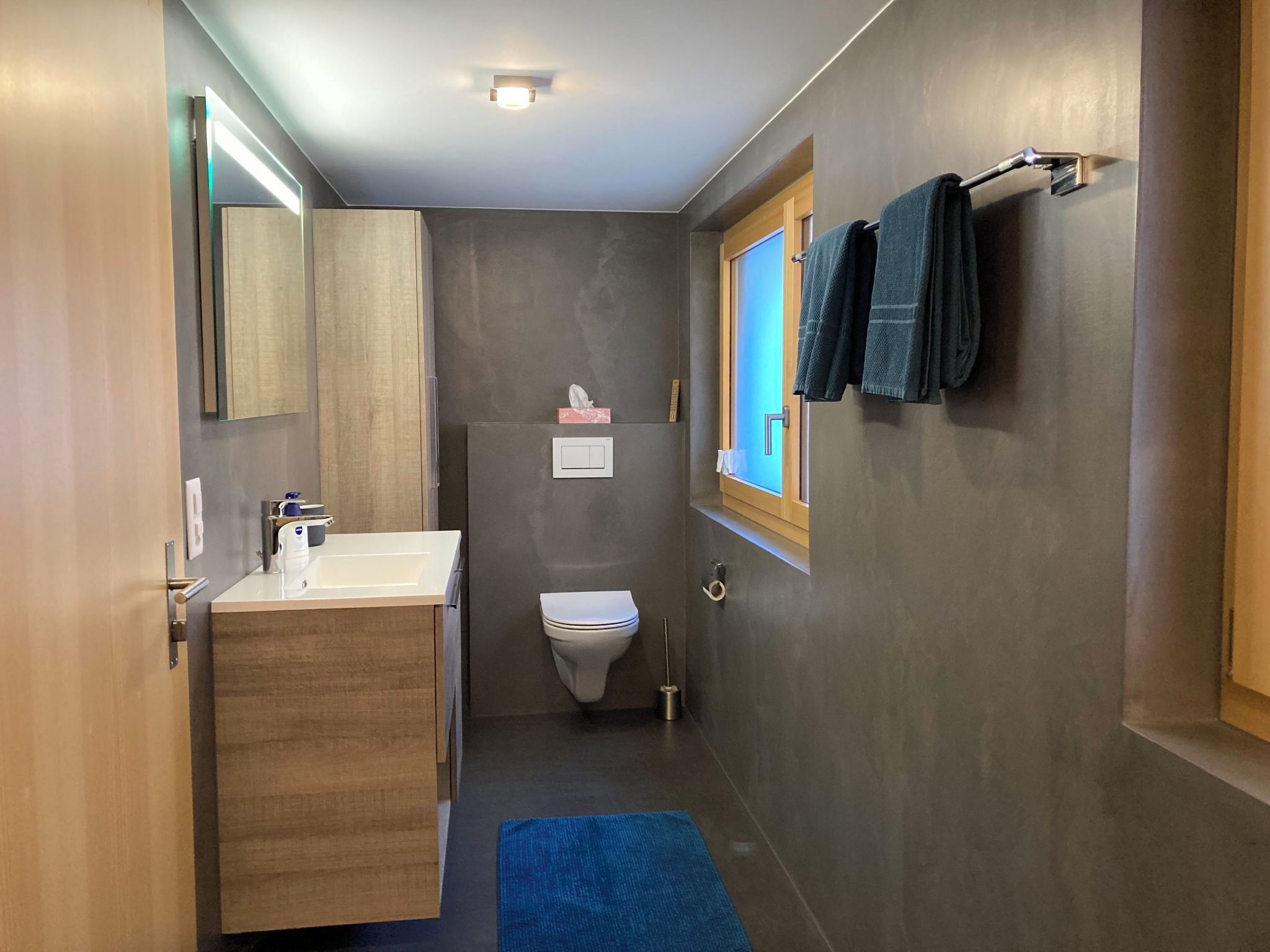 Ein kleines Badezimmer mit einem Holzwaschtisch, einer Toilette und einem Fenster mit Handtüchern.