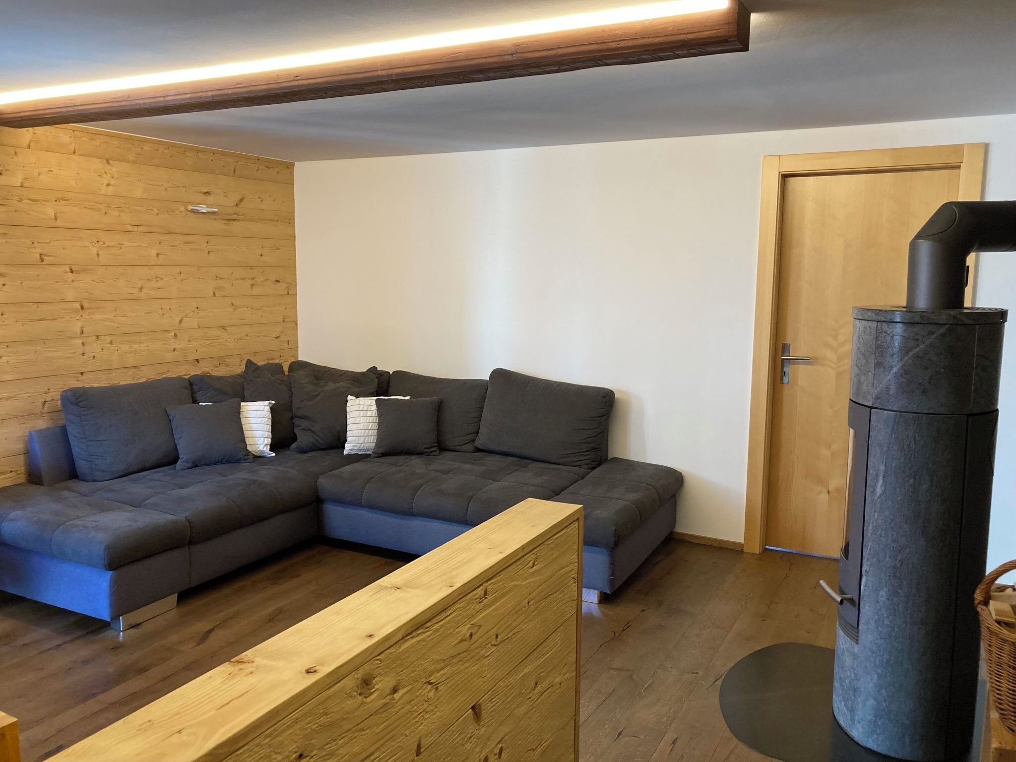 Una sala moderna con un sofá seccional, un panel de madera decorativo y una estufa de leña.