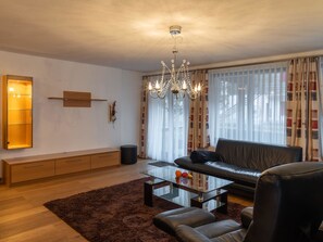 A modern living room with a glass coffee table, leather sofa, and a chandelier. - Villa Alpenhof by Interhome (Saas-Almagell)