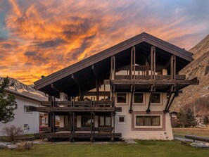A chalet-style building with a wooden balcony, large windows, and a mountainous backdrop. - Villa Alpenhof by Interhome (Saas-Almagell)