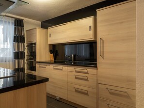 A modern kitchen with wooden cabinets, a black countertop, and stainless steel appliances. - Villa Alpenhof by Interhome (Saas-Almagell)