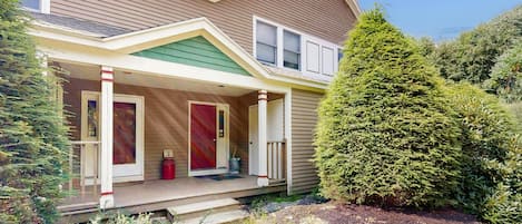A two-story house with a covered porch, a red door, and a green roof.