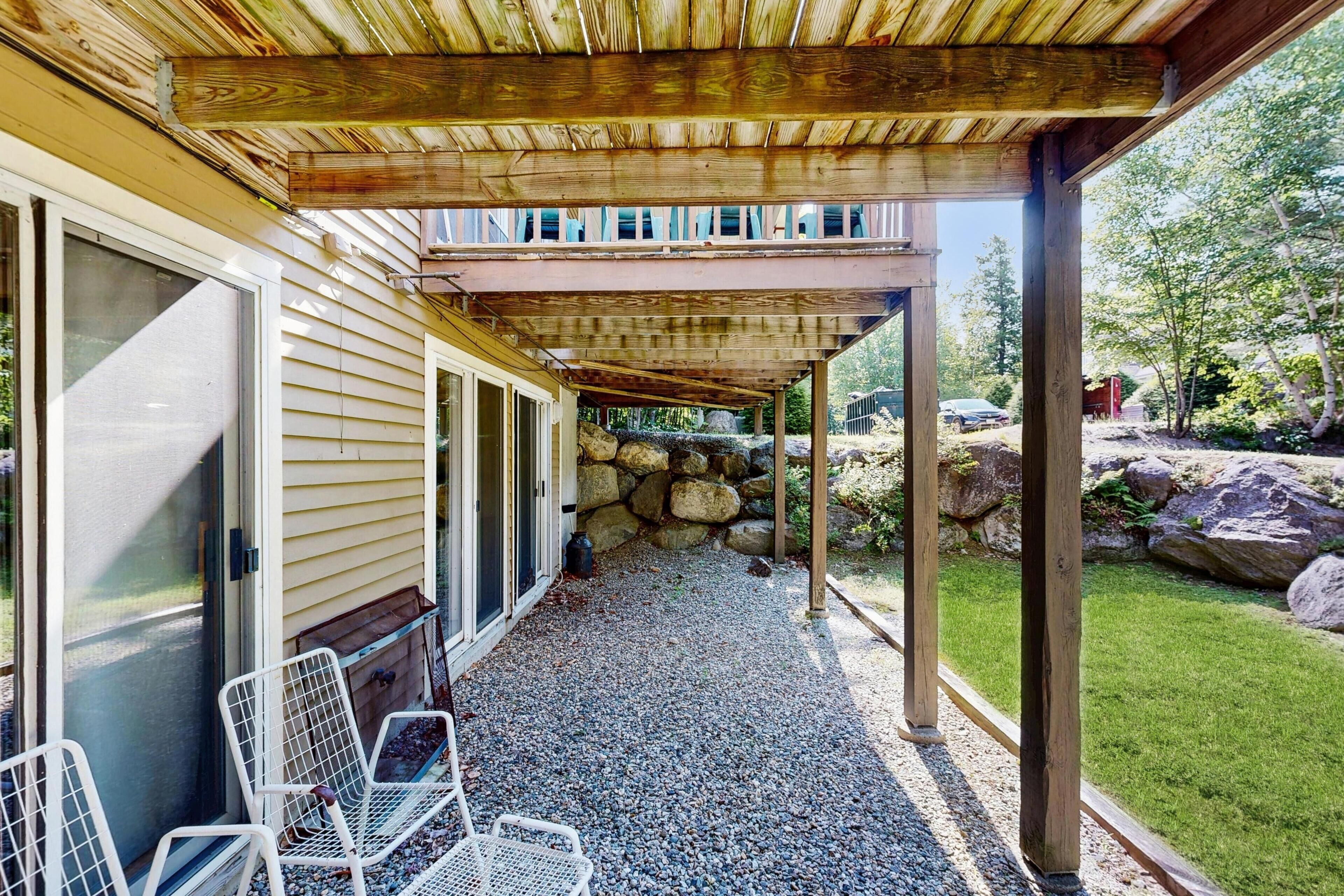 A covered patio area with a stone wall, a gravel floor, and metal chairs.