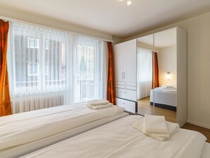 A hotel room with two beds, a large mirror, a wardrobe, and a bathroom with a sink and mirror. - Haus City by Interhome (Saas-Grund)