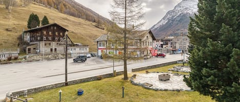 A mountain village with traditional wooden buildings, a paved road, and a parking area.