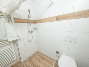 Un baño pequeño y limpio con azulejos blancos, un revestimiento de pared de madera, ducha e inodoro.