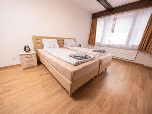 Un dormitorio con cama, mesitas de noche, cómoda y ventana con cortinas.