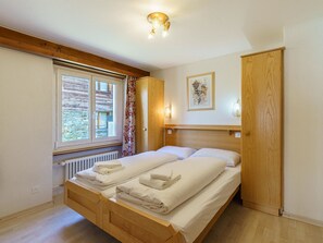 Ein Zimmer mit einem Bett, einem Fenster, einer Heizung und einer Holztür.