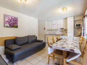 Ein kompakter Wohnbereich mit Sofa, Esstisch, Stühlen, einer Küchenzeile und einem Bild an der Wand.