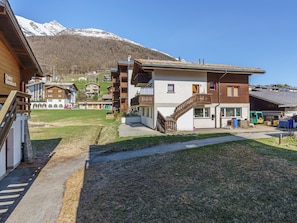 Ein Chalet-Stil-Gebäude mit Holzfassade, einer Treppe und Blick auf verschneite Berge im Hintergrund.