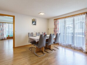 Ein Essbereich mit einem Tisch für vier Personen, Stühlen, einem Gemälde an der Wand und einem Fenster mit Vorhängen.