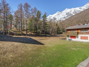 Eine Holzhütte mit rotem Eingang, umgeben von einem Wald und schneebedeckten Bergen im Hintergrund.