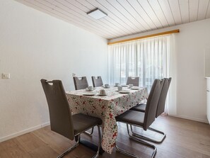 A dining area with a table set for six, surrounded by six chairs, in a room with wooden flooring and white walls. - Haus Slalom by Interhome (Saas-Fee)
