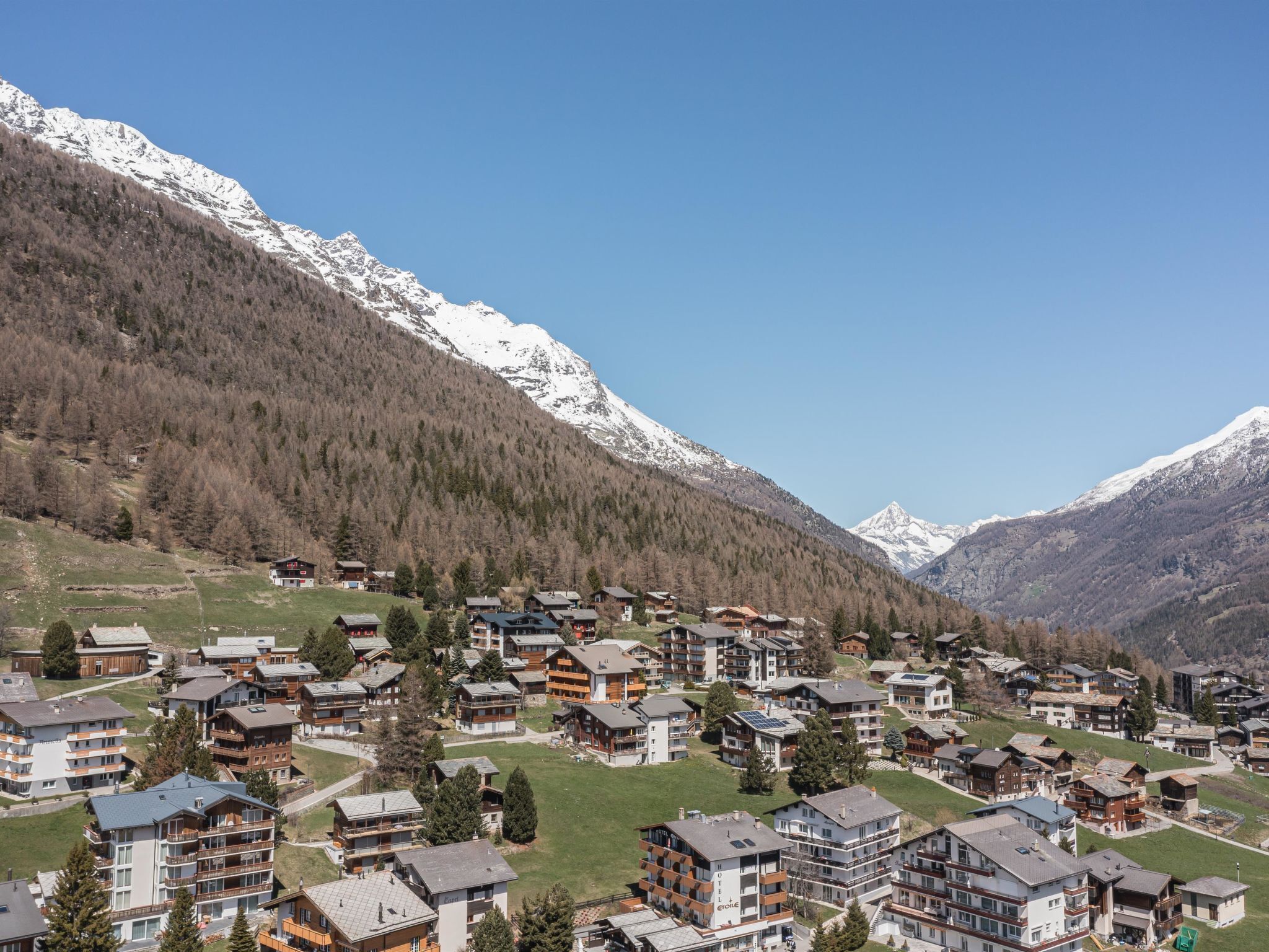 Un village de montagne aux bâtiments de style chalet, une station de ski et, en arrière-plan, des montagnes enneigées.