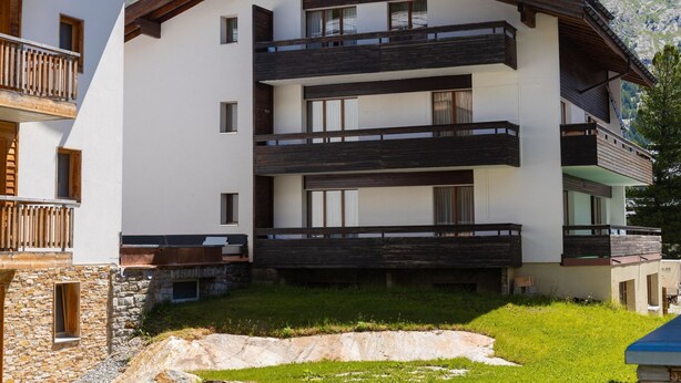 Un edificio a più piani con balconi, fondamenta in pietra e montagne sullo sfondo.