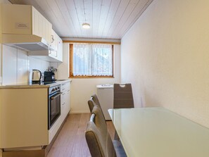 Eine kleine Küche mit weißen Schränken, einem Herd, einem Wasserkocher und einem Fenster mit Spitzenvorhängen.