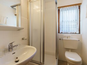 A bathroom with a glass-enclosed shower, a sink with a glass soap dish, and a toilet with a toilet paper holder. - Haus Slalom by Interhome (Saas-Fee)