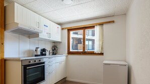A compact kitchen with white cabinets, a built-in oven, a coffee maker, and a window with curtains. - Haus Slalom by Interhome (Saas-Fee)