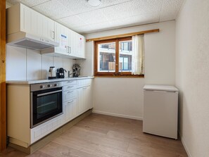 A compact kitchen with white cabinets, a built-in oven, a coffee maker, and a window with curtains. - Haus Slalom by Interhome (Saas-Fee)