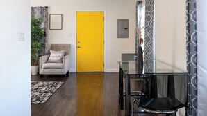 A room with a yellow door, a glass table, a chair, a plant, and a framed sign on the wall. - Cozy getaway (Oakland)