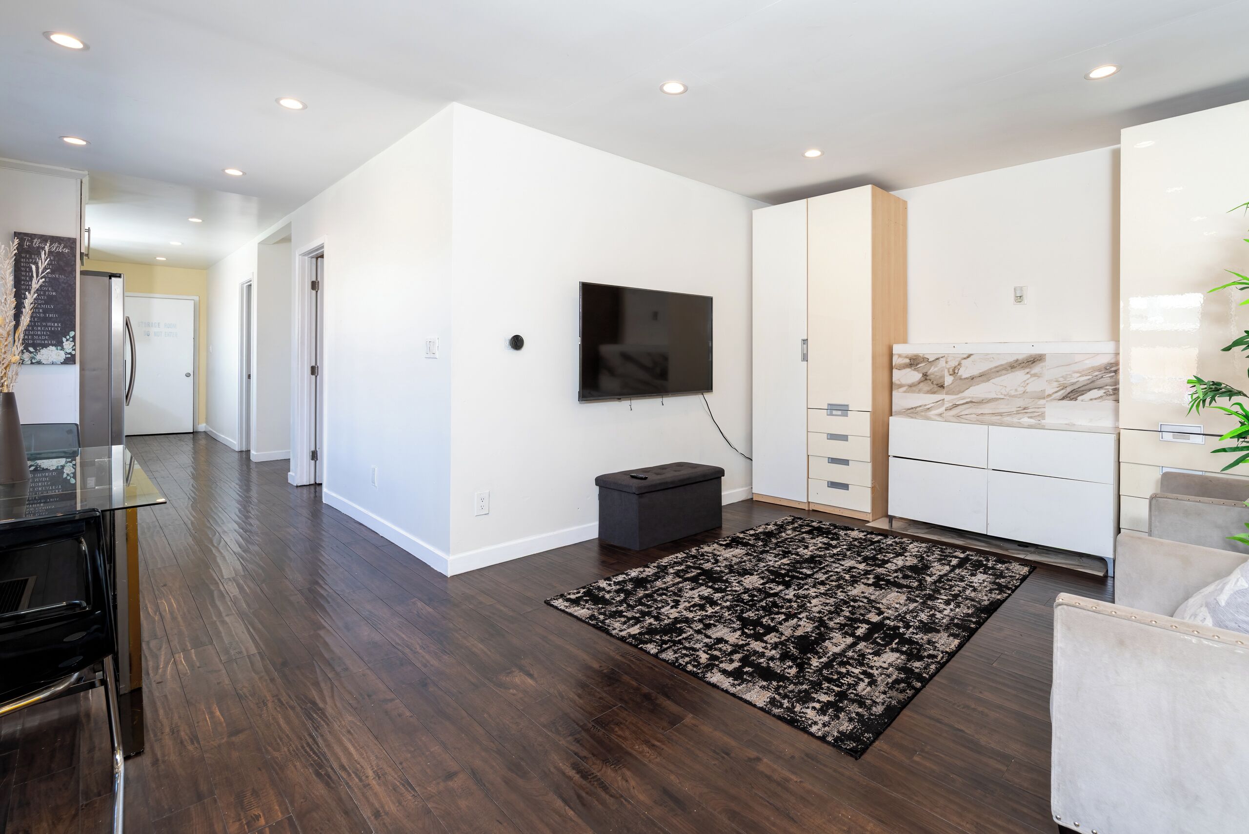 A modern kitchen with a flat-screen TV mounted on the wall, a built-in oven, and a marble backsplash.
