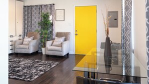 A modern living room with two armchairs, a glass dining table, a yellow door, and a patterned curtain. - Cozy getaway (Oakland)