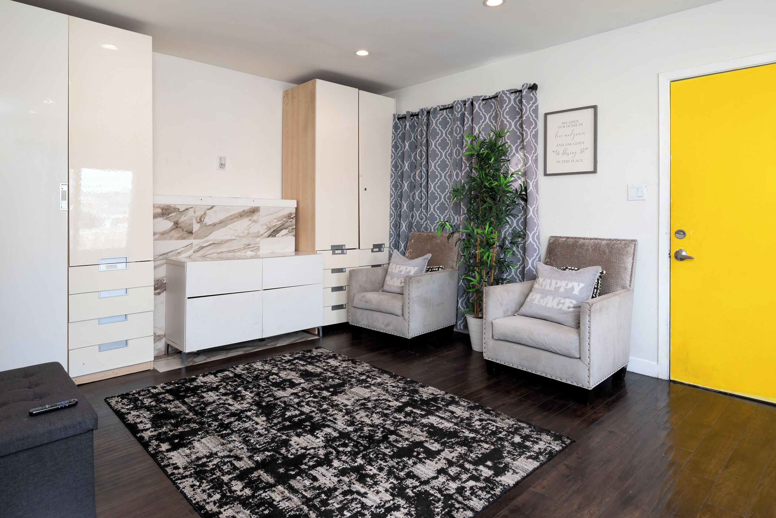 A modern living room with a sofa, armchairs, a coffee table, a marble cabinet, and a yellow door.